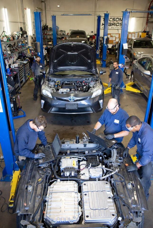 Team of certified mechanics performing hybrid repair in Tucson garage, diagnosing Toyota Prius engine with laptop and tools at Tucson Hybrids Auto Repair